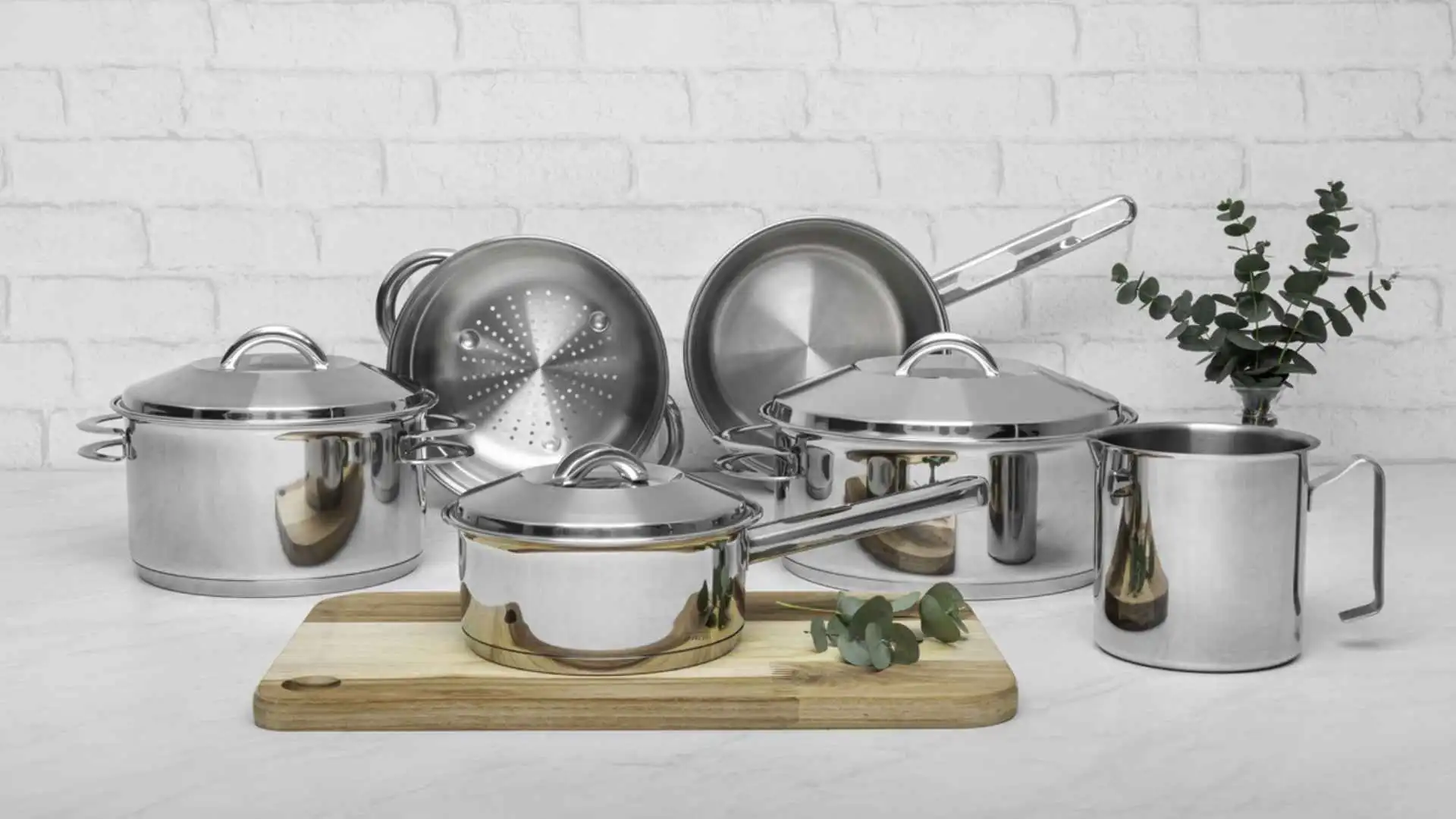 Foto do Jogo de Panelas Tramontina Solar em aço inox com 6 peças exibido sobre uma tábua de madeira em uma cozinha branca