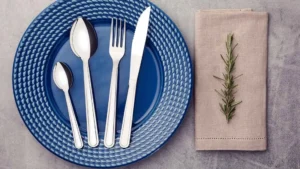 Faqueiro Tramontina Búzios 24 peças em aço inox posicionado sobre prato azul em mesa decorada