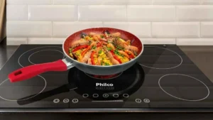 Frigideira Philco PPH240AFR Redstone cinza com cabo vermelho sobre cooktop de indução preto preparando vegetais