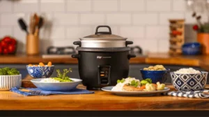 Panela de arroz elétrica WAP WRC1000 preta com tampa de vidro sobre uma bancada de cozinha moderna com pratos servidos ao lado