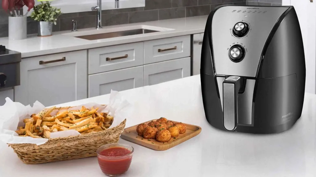 Fritadeira Air Fryer 5L Britânia BFR40PI preta com acabamento em inox posicionada em uma bancada de cozinha moderna ao lado de cestinha de batatas fritas