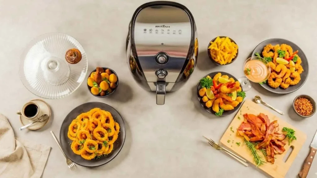 Visão superior da Fritadeira Air Fryer 5L Britânia BFR40PI aberta, cercada por pratos com diversos petiscos preparados sem óleo