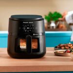 Airfryer Philips Walita NA230 preta sobre uma bancada de madeira em uma cozinha iluminada