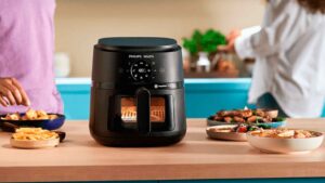 Airfryer Philips Walita NA230 preta sobre uma bancada de madeira em uma cozinha iluminada