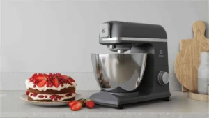 Batedeira Planetária Electrolux KMP70 preta ao lado de um bolo de morango em uma cozinha premium