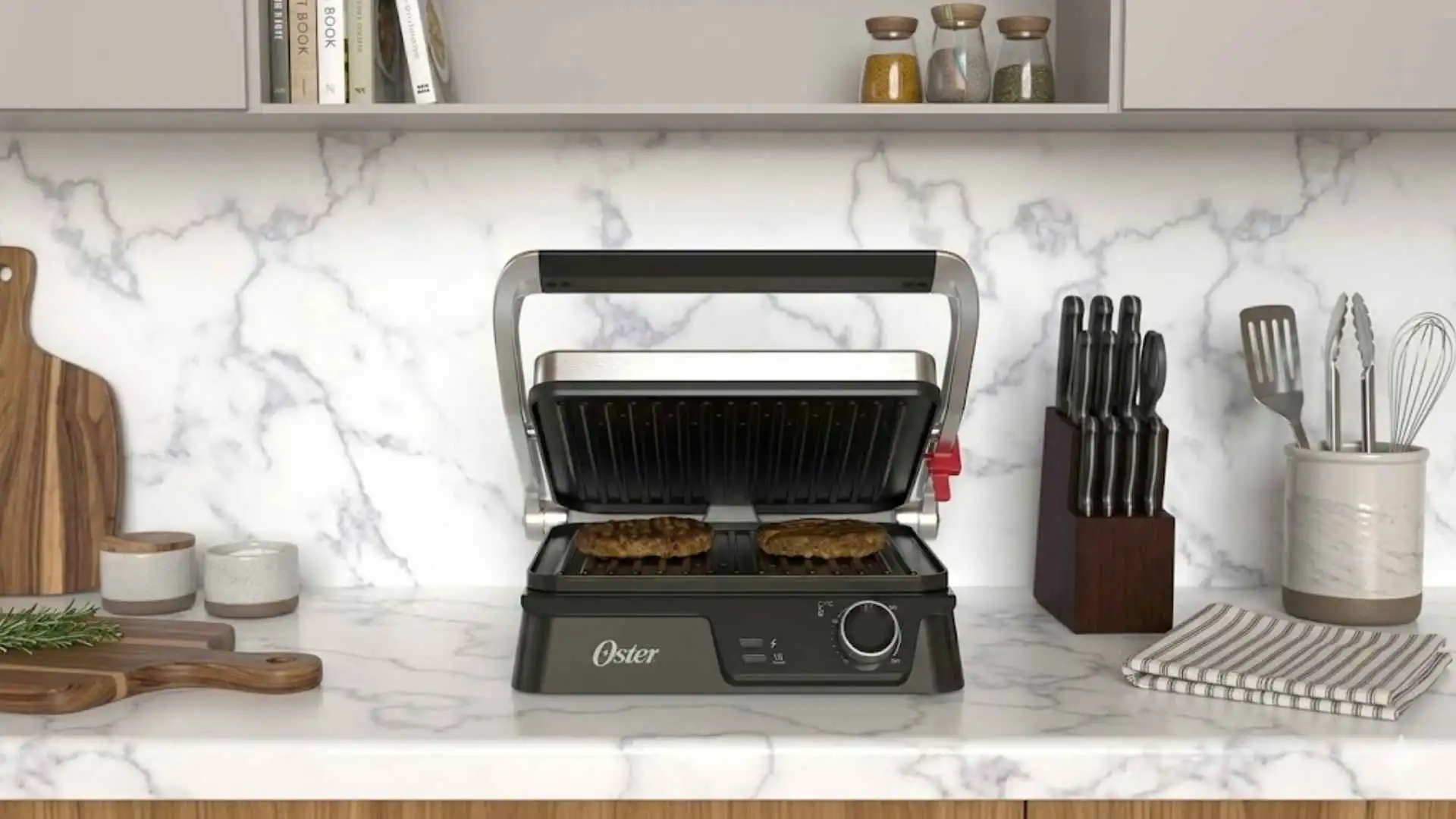 Grill Elétrico Multiuso Oster 2 em 1 em acabamento inox sobre uma bancada de cozinha moderna com azulejos de mármore