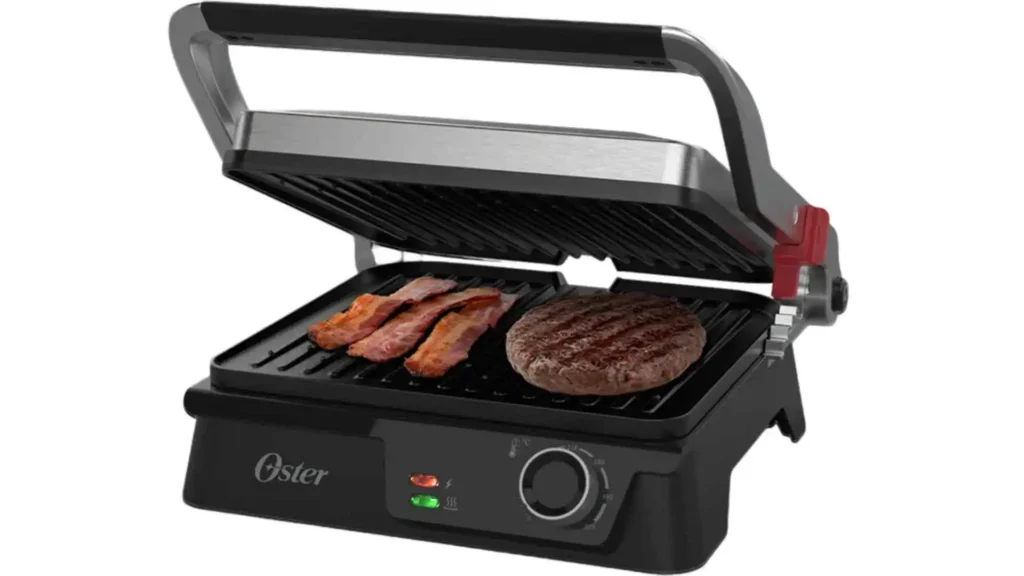 Grill Elétrico Multiuso Oster 2 em 1 grelhando um bife alto e tiras de bacon, destacando as chapas caneladas e a alça ergonômica
