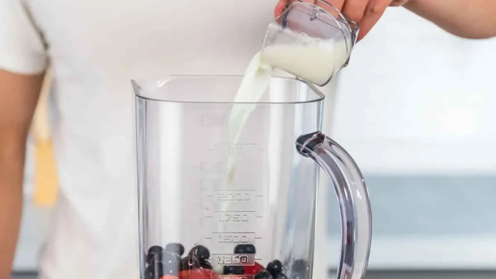 Pessoa utilizando a sobretampa dosadora do liquidificador Britânia BLQ1300P para adicionar leite durante o preparo