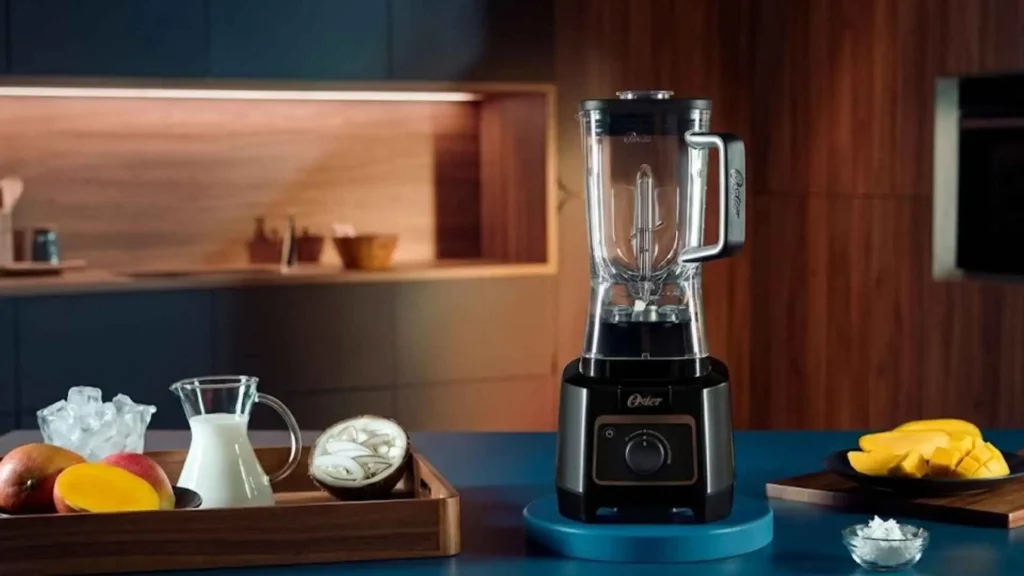 Liquidificador Oster Xtreme Mix em uma bancada de cozinha com ingredientes como leite e frutas tropicais