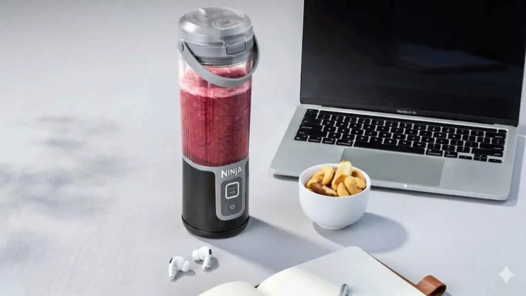 Ninja Blast Liquidificador Portátil Bivolt preto em uma mesa de escritório com notebook, preparando um smoothie de frutas vermelhas