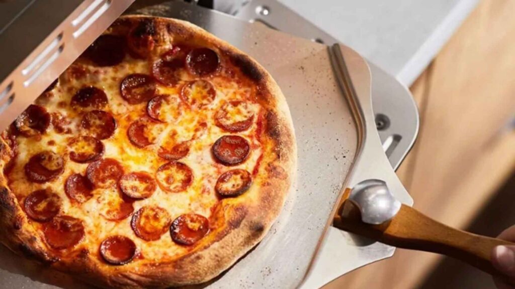 Pizza de pepperoni com borda dourada e crocante sendo retirada do Forno de Pizza Cuisinart CPZ-120BR com a pá oficial