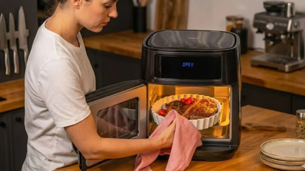Pessoa utilizando a luz interna e visor da WAP Airfry Oven Digital Black para monitorar o preparo de uma receita em travessa de cerâmica