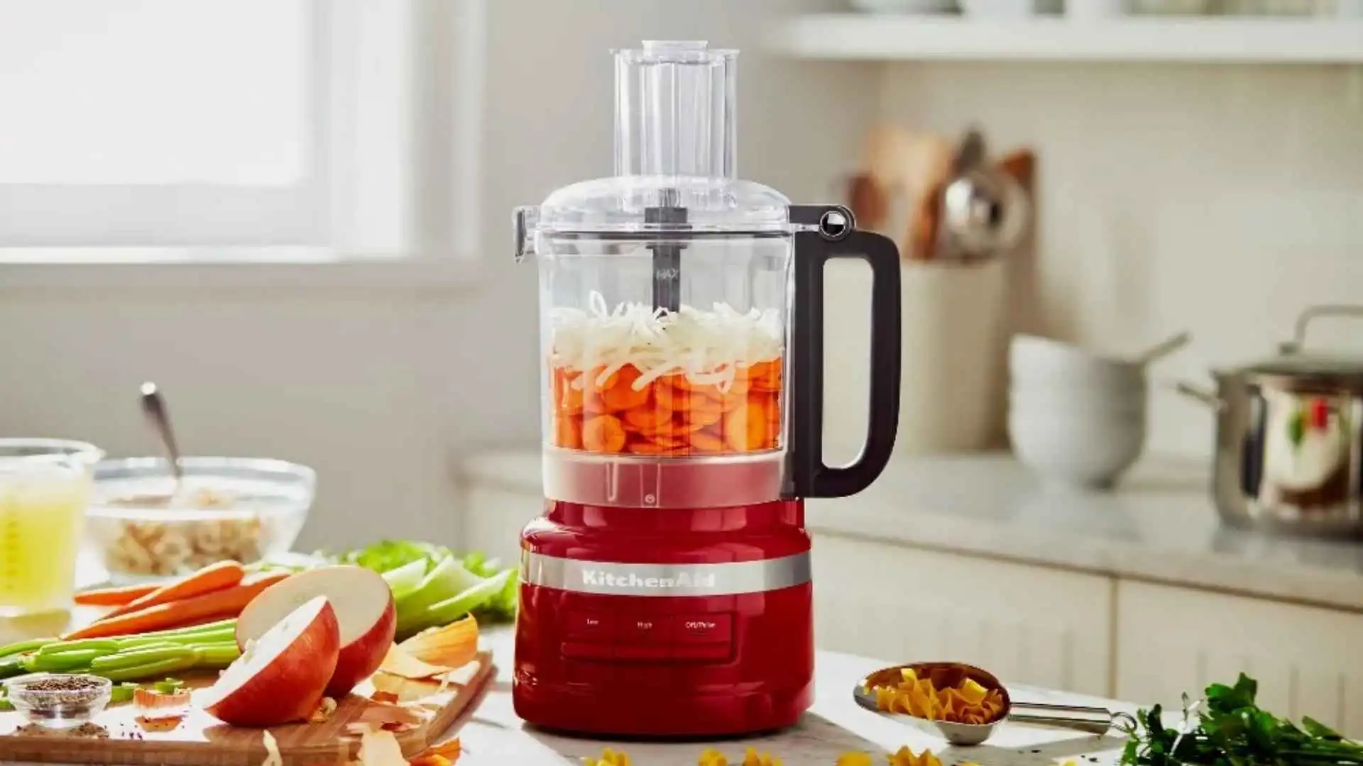 Processador KitchenAid 2.1L Empire Red fatiando cenouras com precisão em uma bancada de cozinha