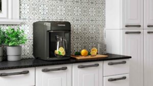 Purificador de água Colormaq Acqua na cor grafito instalado sobre uma bancada de cozinha moderna com armários brancos