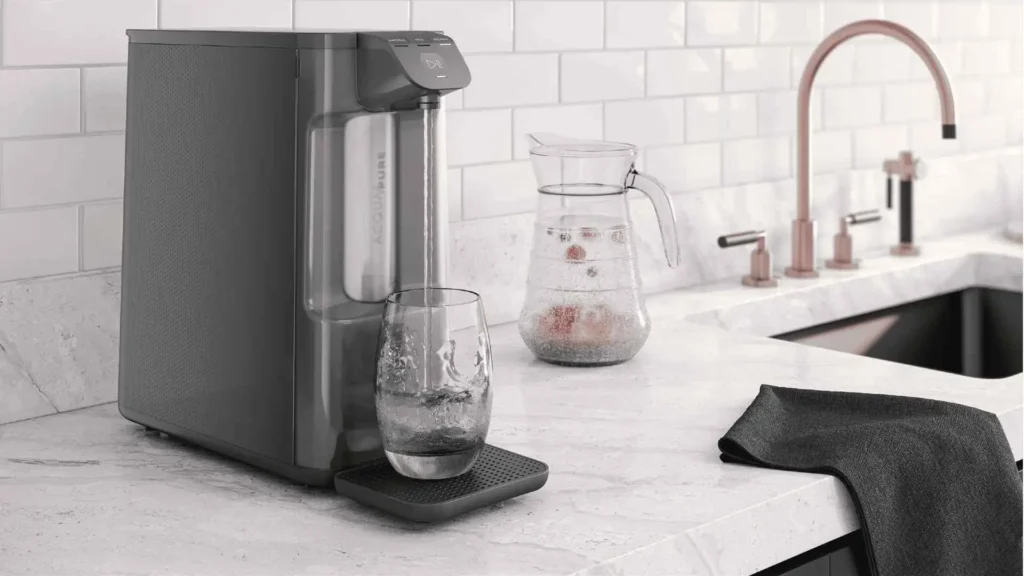 Purificador de água Electrolux PE12G cinza grafite instalado em bancada de cozinha moderna, destacando seu design compacto