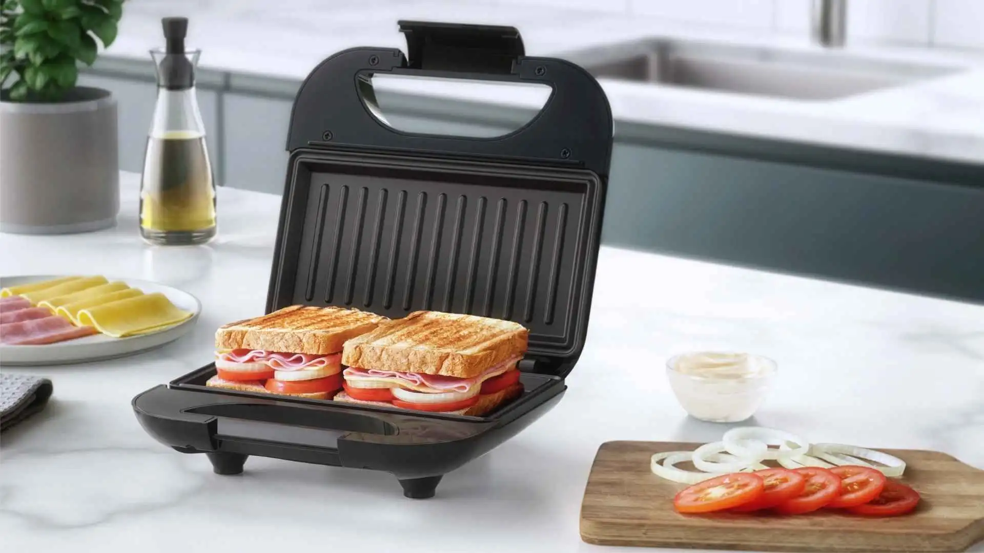 Sanduicheira Grill Electrolux ESG20 aberta com dois sanduíches de presunto e queijo sendo preparados em uma cozinha moderna