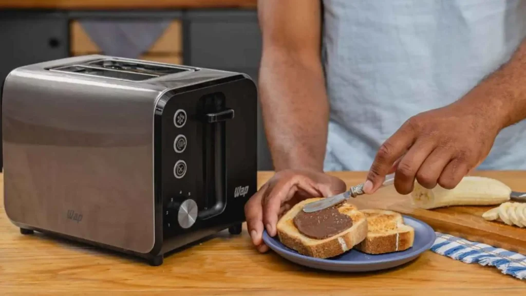 Pessoa utilizando a Torradeira Elétrica WAP WTE1 para preparar fatias de pão com geleia