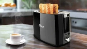 Torradeira Oster Black Simple Life preta em uma bancada de cozinha com fatias de pão torradas e uma xícara de café