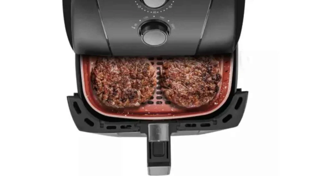 Duas postas de carne grelhando dentro do cesto quadrado com revestimento cerâmico da Air Fryer Britânia 5,5L BFR50