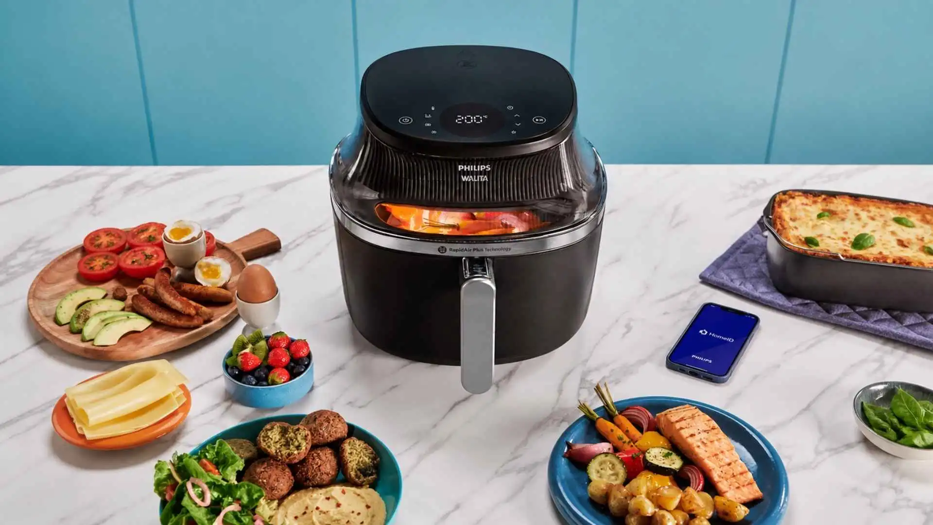 Fritadeira Airfryer Philips Walita Série 3000 XL Digital Preta NA341 sobre uma bancada com diversas porções de alimentos e acessórios de cozinha