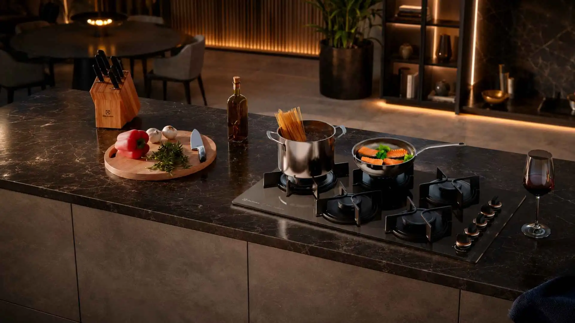 Visão ampla de uma cozinha planejada moderna com o Cooktop 5 Bocas Electrolux Pro Series KE5PS embutido em uma bancada de granito escuro iluminada