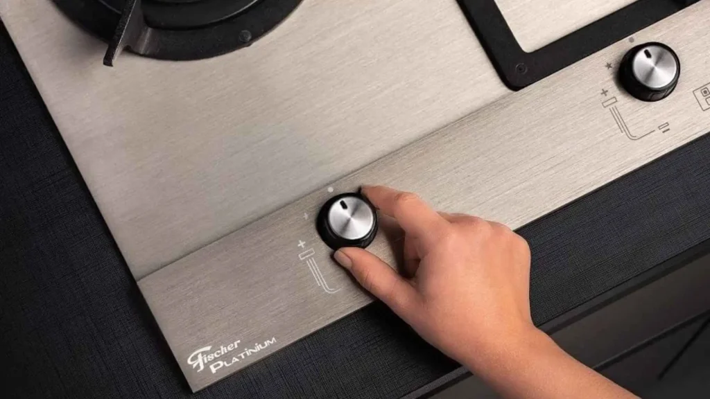 Mão girando o botão com acendimento superautomático na mesa de aço inox do cooktop a gás Fischer Platinium Prime