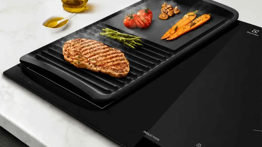 Grelhado de carne e vegetais sendo preparado em chapa retangular utilizando a tecnologia Unicook do Cooktop de Indução Electrolux IE60P