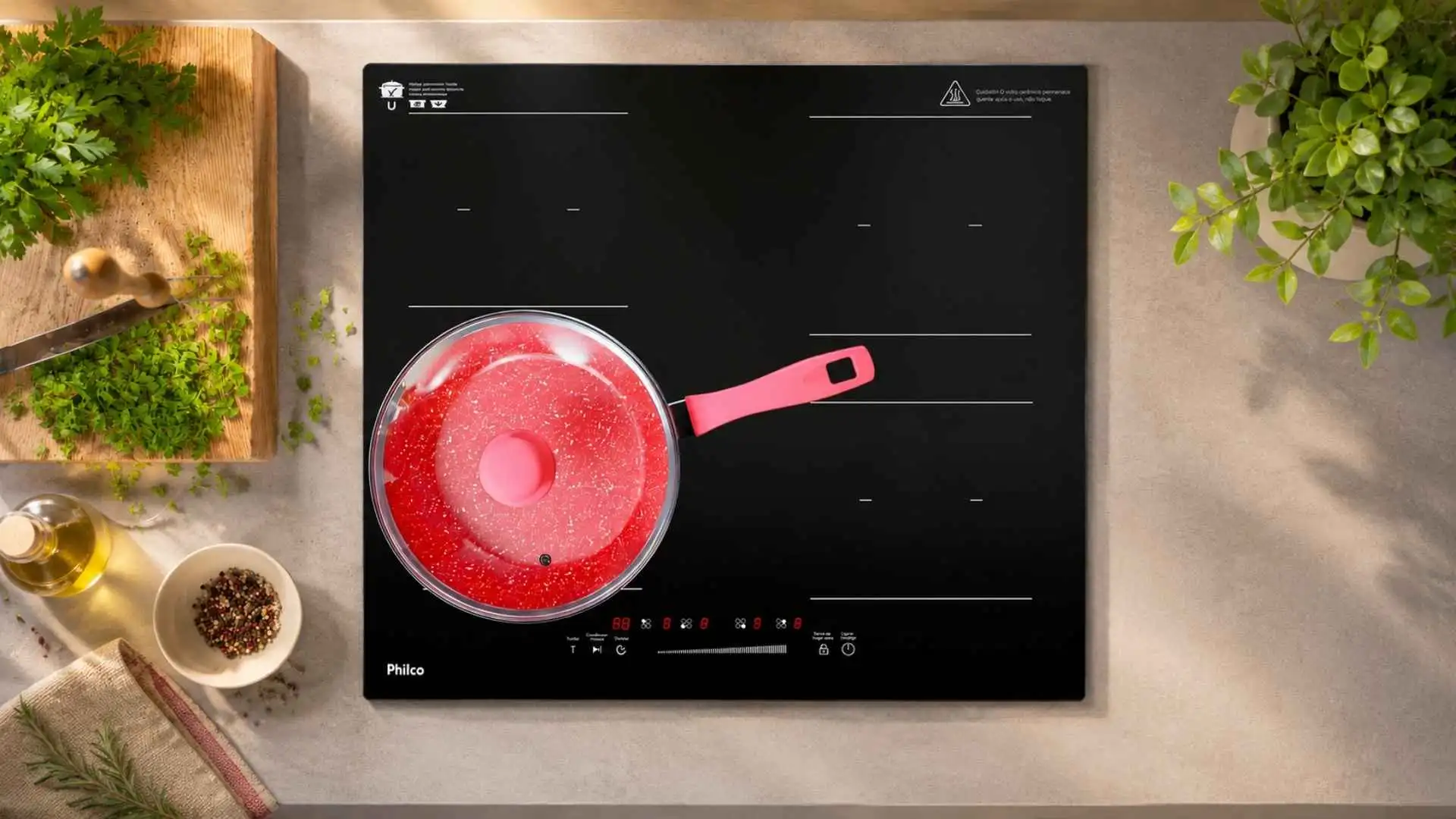 Vista superior de um cooktop de indução Philco PCTQ1 com uma panela vermelha posicionada sobre uma das zonas de aquecimento ligadas