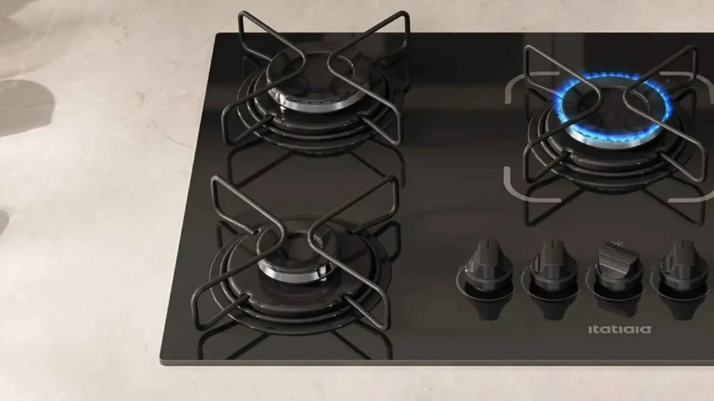 Close-up das grades individuais esmaltadas e dos queimadores acesos do cooktop a gás Itatiaia 5 bocas Essencial