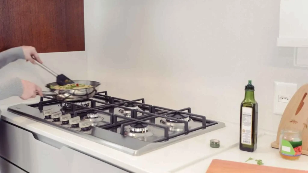 Pessoa utilizando panela sobre o queimador aceso do cooktop Tramontina Penta Plus em uma bancada de cozinha