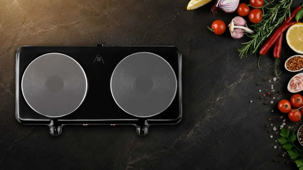 Vista superior de um fogão elétrico cooktop 2 bocas Elgin preto ao lado de temperos e vegetais frescos