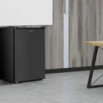 Frigobar Philco 68L PFG85P na cor preta instalado de forma compacta abaixo de um balcão em ambiente de escritório ou sala de estar