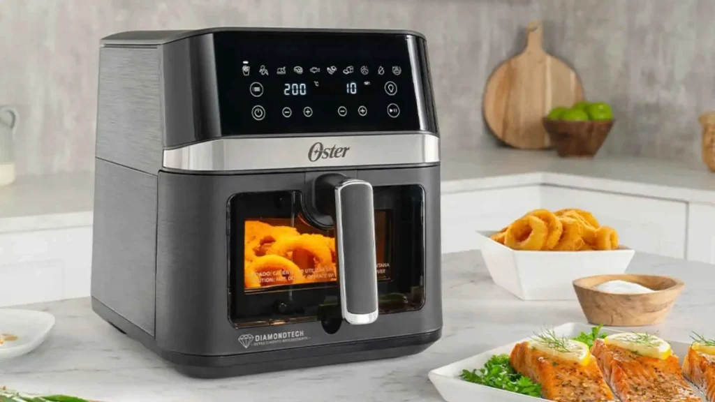 Fritadeira DiamondTech Oster 6L preta com visor transparente preparando frango e batatas em uma cozinha moderna