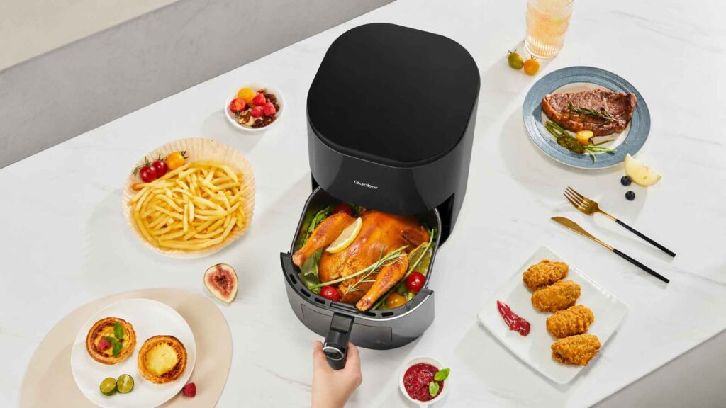 Cesto aberto da Air Fryer Gaabor Duo Digital mostrando um frango assado inteiro e dourado ao lado de pratos com batatas fritas e petiscos