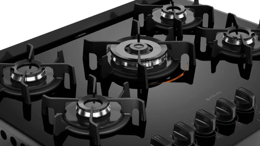 Detalhe aproximado da mesa de vidro temperado preto e das trempes de ferro fundido do fogão Atlas U Top de 5 bocas